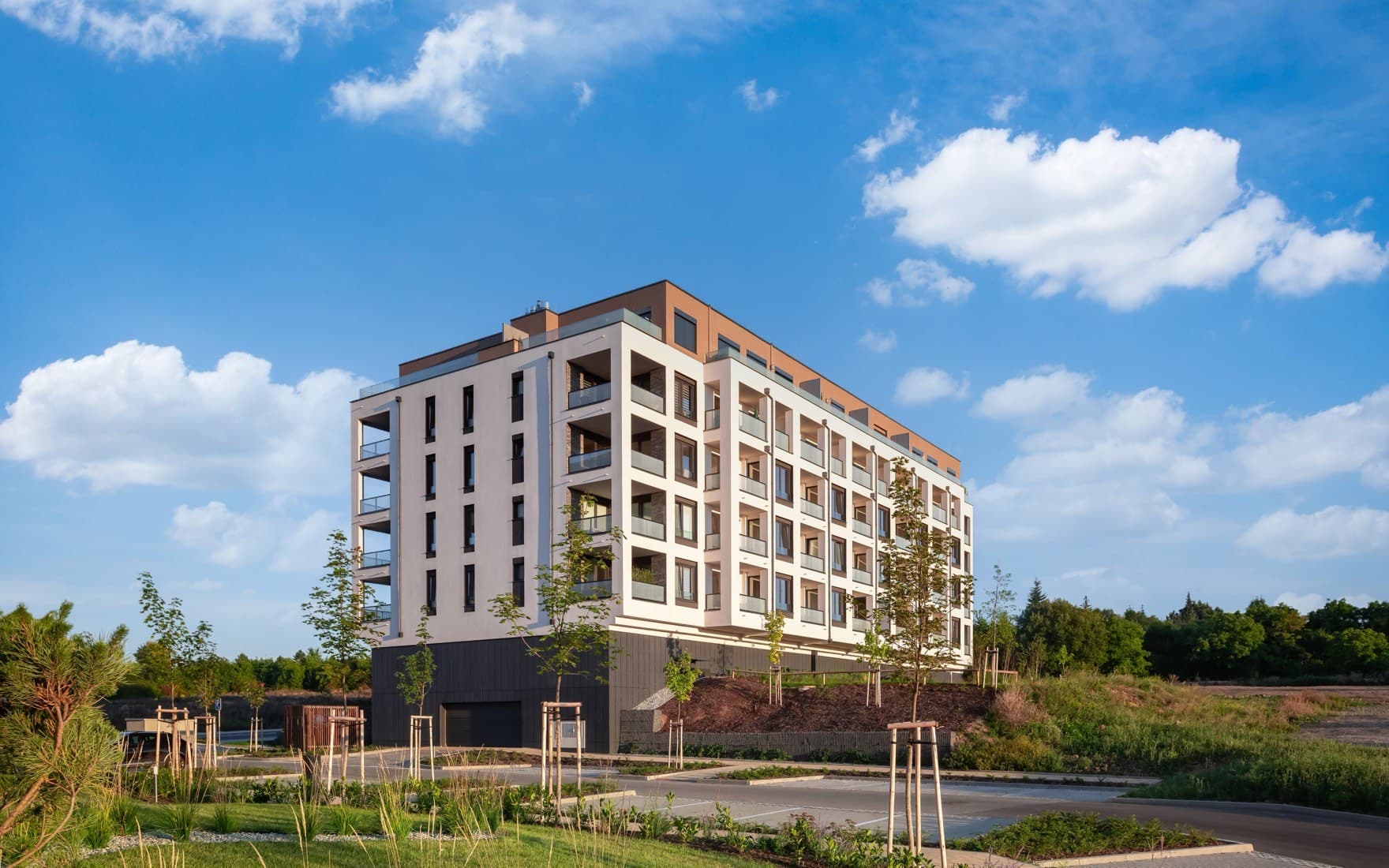 Mid-rise residential apartment building with landscaped grounds under clear sky